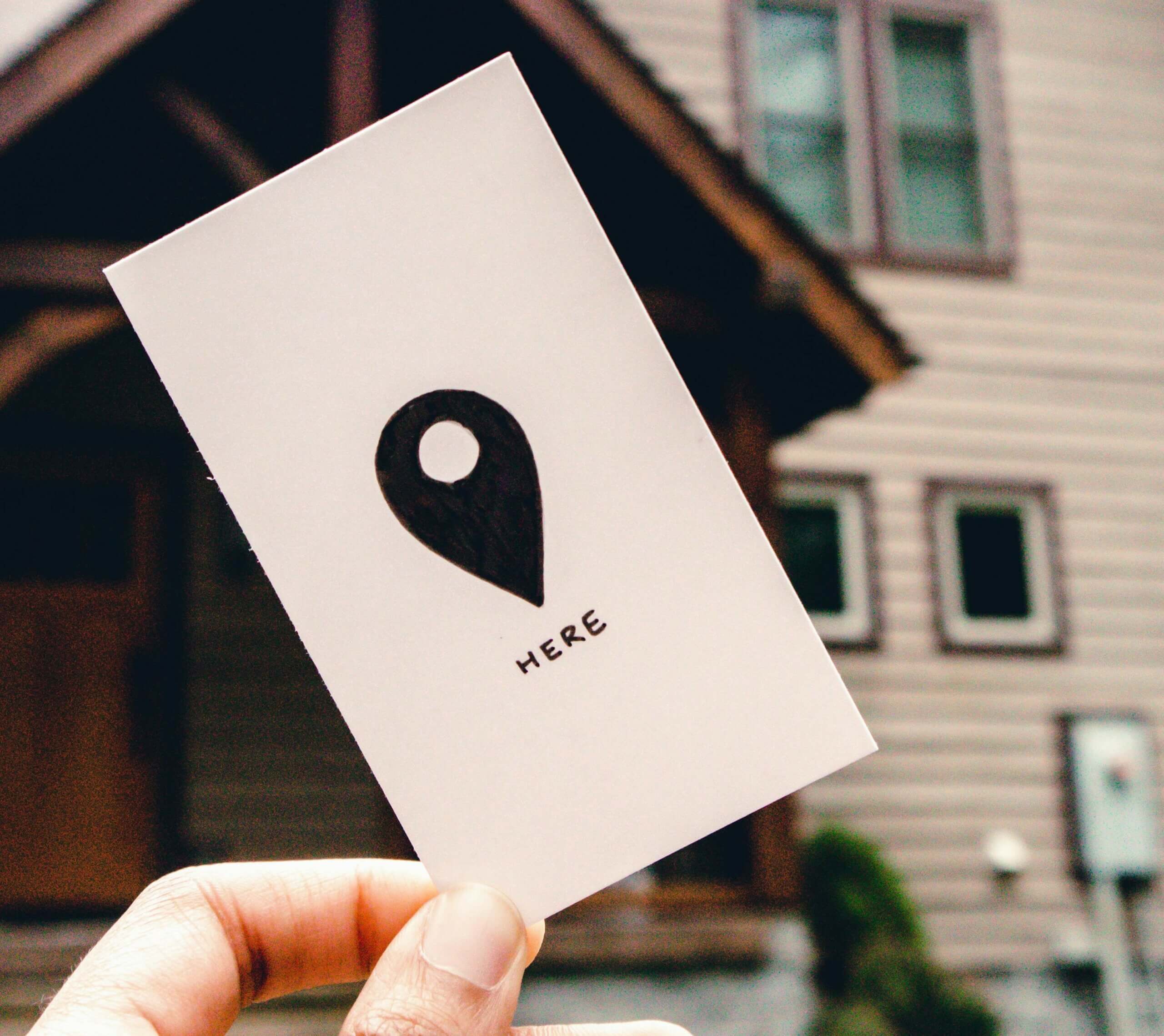 photo d'une personne tenant un carton avec un dessin du symbole représentant l'épingle google map devant sont entreprise